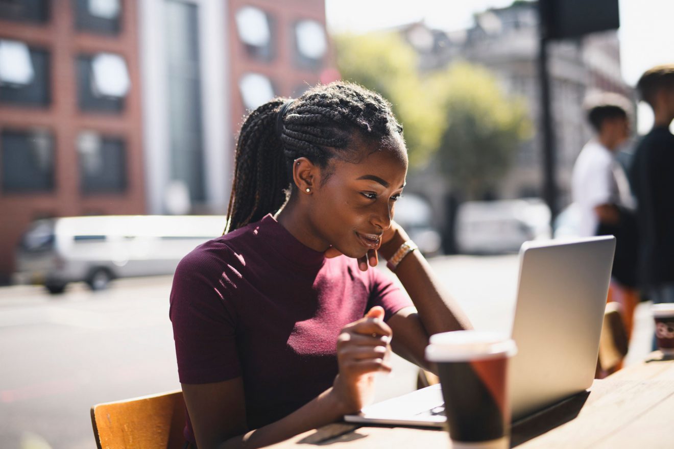 A smiling woman sitting at an outdoor table in front of a laptop.