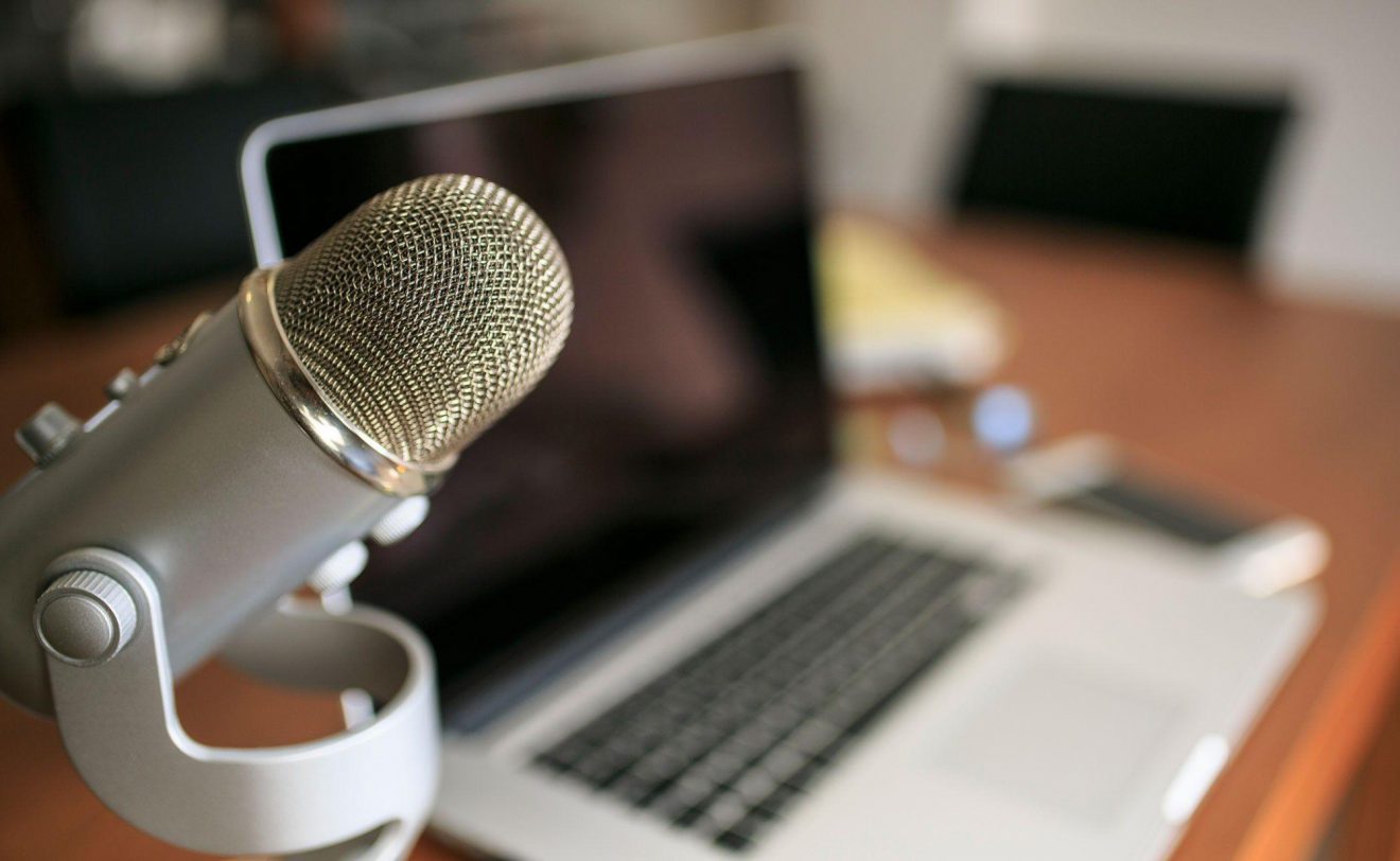 A tabletop microphone sits at a desk in front of a laptop.