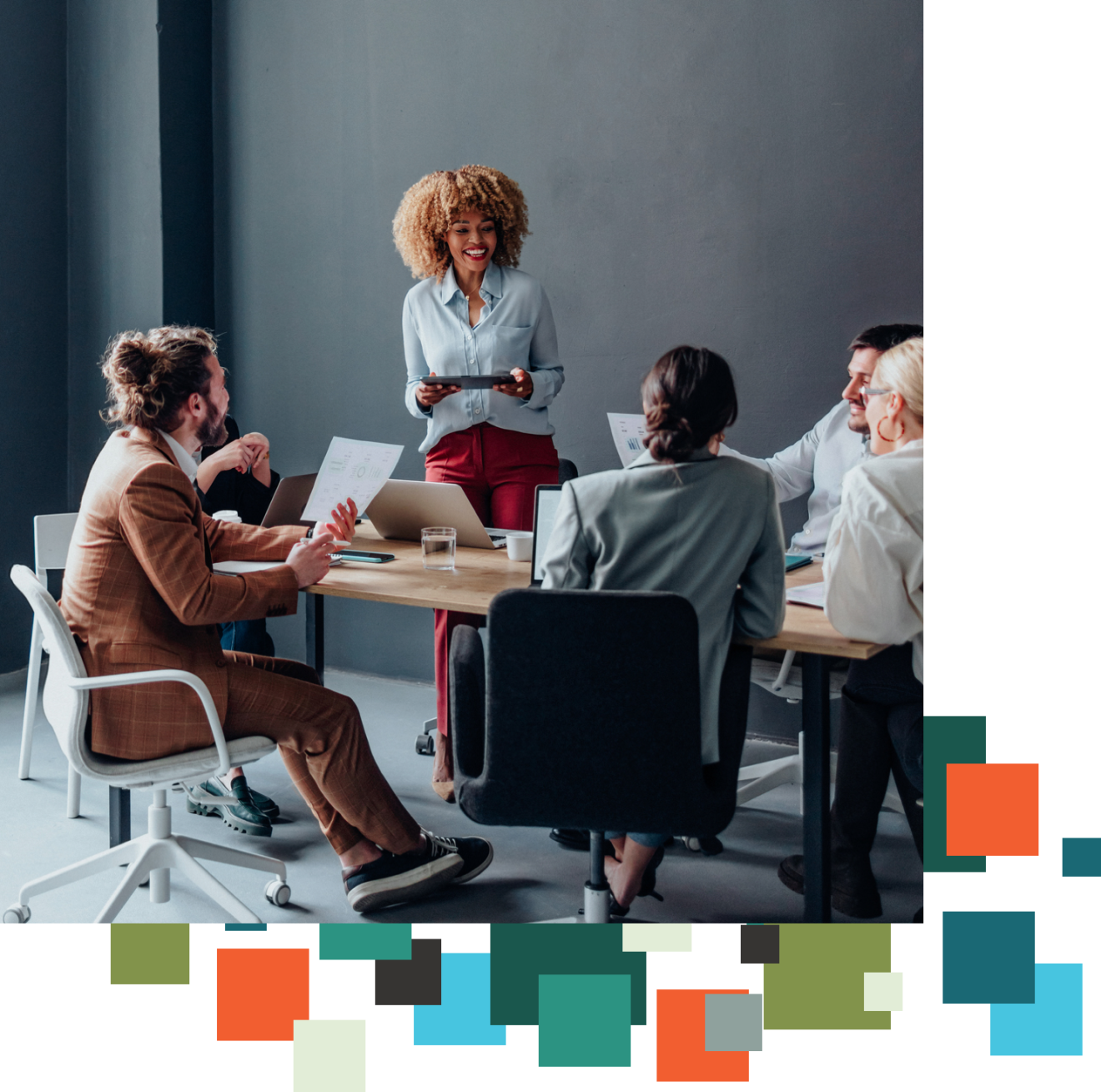 A woman, standing, leads a conversation around a table of other people